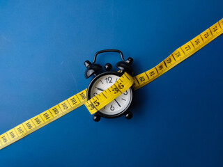 Yellow measuring tape and alarm clock on a blue background.