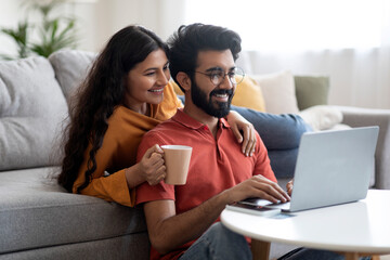 Home Leisure. Indian Couple Relaxing With Laptop And Coffee In Living Room