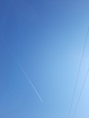 An airplane flying in an empty sky at midday hour on a spring day. Power lines in a photo taken from the ground.