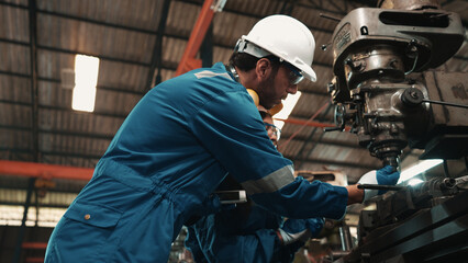 African factory worker in safety wear is checking a piece of industrial metal while Caucasian coworker help her to combine metal part to machine. Two production engineers are working in metal factory.