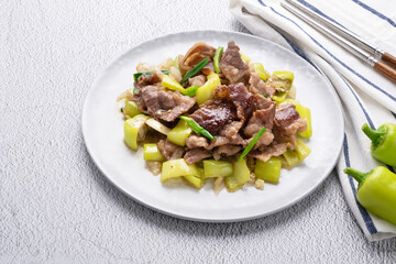 Stir fried green pepper with brisket sliced in white dish on concrete table.