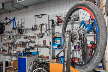 Blue bicycle wheel holder mounted on table for repairing bicycle equipment in workshop. Against background of wall with tools blue rack with bicycle wheel is depicted, bicycle chain lies next to it