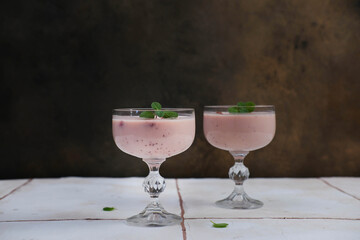Two glasses with strawberries puding on white table in brown background.