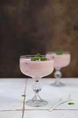 Two glasses with strawberries puding on white table in brown background.