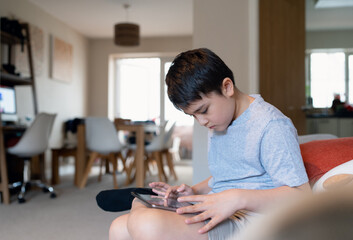 Fototapeta premium Education concept,School kid using tablet reading story from internet,Boy studying online learning at home,Child holding digital pad using wifi playing game or chatting with friends.Back to School