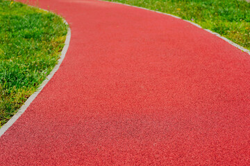 padded rubber sport and running track floor in selective focus. blurred background. green grass on the sides. workout and leisure activities concept. fine granular texture.