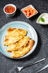 Russian thin pancakes or blini with red caviar nd salmon on black table