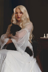 Young woman in a vintage white dress sitting in a room with a black Maine-Coon cat.