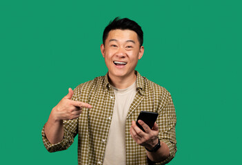 Cool mobile offer. Excited korean middle aged man pointing at smartphone, reacting to new app,...
