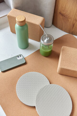 Home fitness flat lay. Top view of brown karemat yoga blocks smartphone bottle with water and green...
