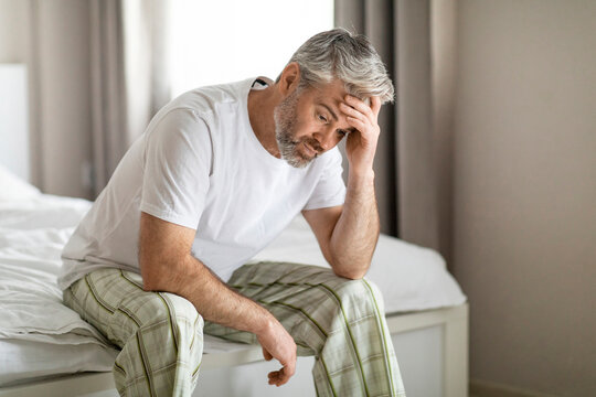 Upset Middle Aged Man Sitting On Bed Alone At Home