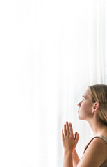 Concentrated beautiful girl sits and looks out the window at home. Woman sadly contemplatively looks out the window alone..