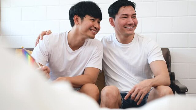 Asian LGBTQ gay couple wearing white t-shirt smiling with happy face holding rainbow flag, gay pride or LGBTQ concept	