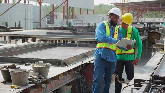 Young African American foreman and worker examining and check produce precast walls while looking document in factory industrial, manager and labor check quality of cement wall, industry concept.