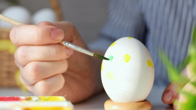 Happy Easter concept. Close-up of a young womans hand draws a colorful pattern on a chicken egg with a brush and paints. Decoration for the spring holiday. Preparation for the celebration.