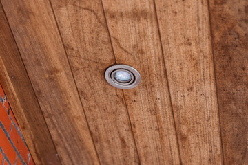 A portrait of a weather sealed light spot put in the wooden planks of a roof overhang. The lamp is...
