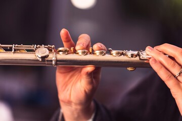 A portrait of the fingers of a hand of a flutist musician gripping down on the valves of a metal...