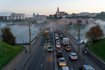 Belarus, Grodno July 15, 2022: The movement of cars and public transport on the bridge over the river. Thick morning fog over the bridge in the city. fog over a crowded road