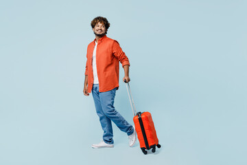 Traveler Indian man wear casual clothes hold suitcase walk go isolated on plain pastel light blue cyan background Tourist travel abroad in free spare time rest getaway Air flight trip journey concept