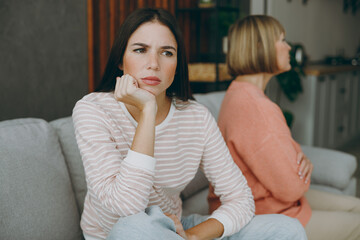 Two sad pensive depressed unhappy upset adult women mature mom young kid wearing casual clothes sit on gray sofa couch stay at home flat rest relax spend free spare time in living room Family concept