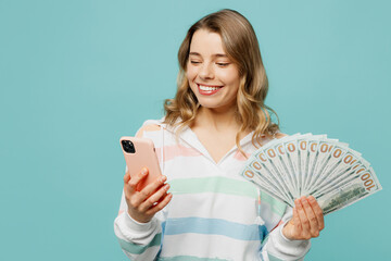 Young blonde woman wear striped hoody use mobile cell phone hold in hand fan of cash money in...