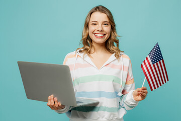 Young smiling fun IT woman wear striped hoody hold American flag use work on laptop pc computer chatting study online isolated on plain pastel blue cyan background studio portrait. Lifestyle concept.