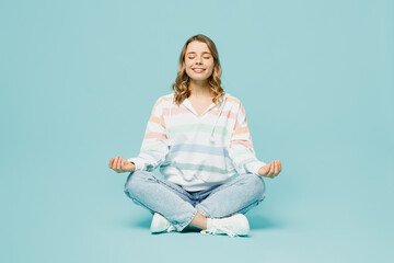 Full body young spiritual tranquil woman wearing striped hoody sitting hold spreading hands in yoga...