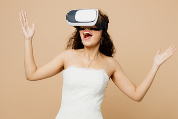 Happy excited beautiful young woman bride wear wedding dress posing watching in vr headset pc gadget isolated on plain pastel light beige background studio portrait Ceremony celebration party concept