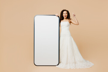 Full body happy young woman bride wear wedding dress posing big huge blank screen mobile cell phone...
