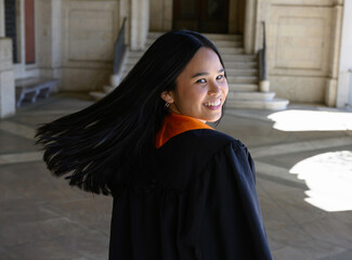 Young attractive Asian American college student, wearing gown and sash, celebrating her graduation from the university