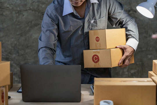 Asian Male SME Small Business Entrepreneur, freelance working from home using laptop for commercial auditing. online marketing Packaging Box SME Seller Concept Ecommerce Team online sales