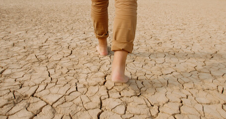 Close up shot of feet of adult man walking barefoot on bottom of dried lake or river, stepping on...