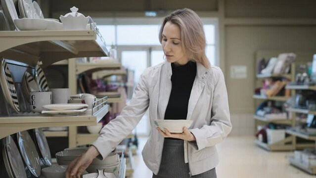A young woman in a kitchen goods store chooses new dishes for the house. The buyer examines the plates.