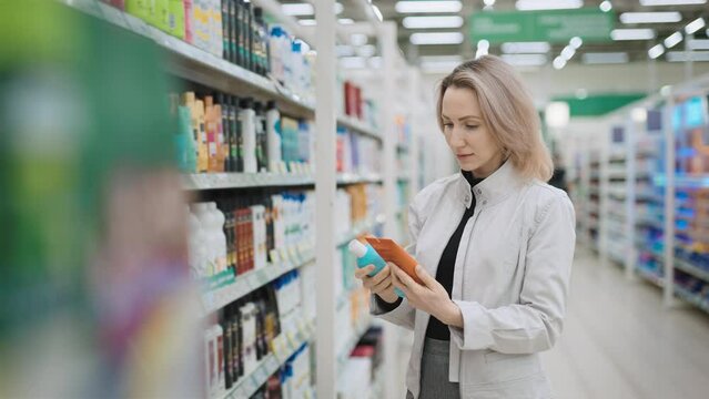 Happy young woman chooses a hair care product. A customer in a supermarket picks up shampoo and conditioner