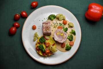 Meat roll with broccoli, white cabbage, carrots, and mashed potatoes in a white plate on a dark green background.