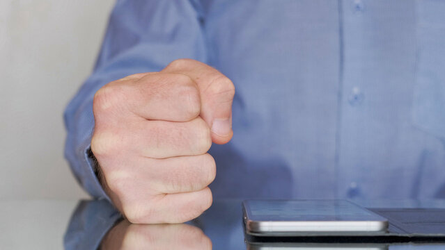 Close-up shot of a boss clenching his fist signaling anger and frustration as his hand rests on an office table. Disgruntled boss at a meeting.