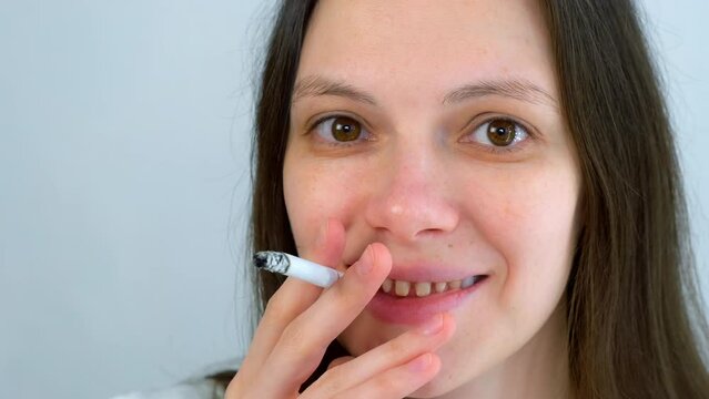 Young woman with yellow bad teeth smoking a cigarrete and smiling looking at camera. Bad habits for dental health, destructive effect of smoking. Ugly smile. Dentistry treatment, prosthetics of teeth.