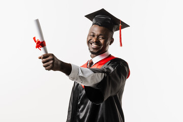 Happy african student in black graduation gown and cap raises masters degree diploma above head on...