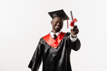 Happy african student in black graduation gown and cap raises masters degree diploma above head on...