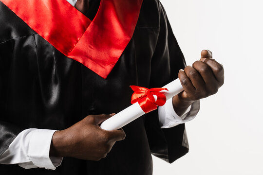 Masters degree diploma with red ribbon in hands of graduate african man in black graduation gown on white background. Graduate african is graduating high school and celebrating academic achievement.