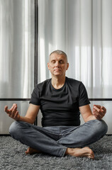 Fototapeta premium A man meditates in the lotus position on a yoga mat during a break from work.