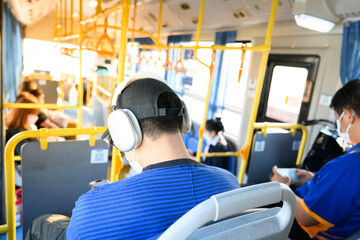 A man wearing cap on the passenger seat of the bus listens to music.Traveler sitting outside the window public transportation.Tourist is traveling and looking through the bus window.