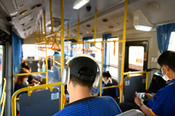 Fototapeta na wymiar A man wearing cap on the passenger seat of the bus listens to music.Traveler sitting outside the window public transportation.Tourist is traveling and looking through the bus window.