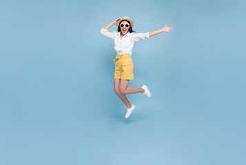 Fototapeta na wymiar Happy smiling young Asian tourist woman jumping to summer time isolated on blue studio background. copy space