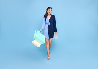 beautiful smiling Asian shopaholic woman holding shopping bags walking to shop summer sale on blue studio background. - obrazy, fototapety, plakaty