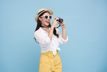 Happy smiling young asian woman tourist in summer hat standing with camera taking photo isolated on blue studio background - obrazy, fototapety, plakaty