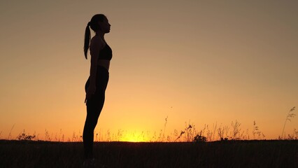 Girl is engaged in gymnastics. Athlete exercising in nature. Young woman goes in for sports in park at sunset. Healthy girl is engaged in fitness, outside city in sun. Workout and warm-up in outdoors