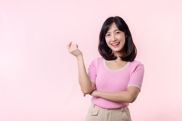 Portrait young beautiful asian woman happy smile pointing finger and hand to showing on copy space isolated on pink background. Attractive female person gesture attention to this promotion.