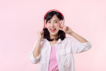 Smile pretty asian model person listen music song and enjoy dance with wireless headphone online audio radio sound. Positive fun exited joyful youth female woman on pink isolated background studio