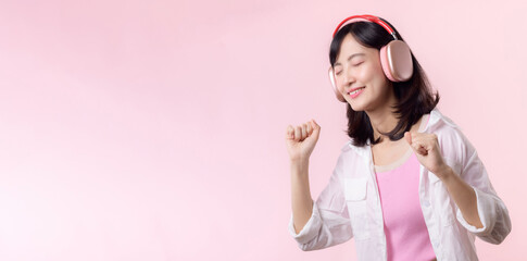 Smile pretty asian model person listen music song and enjoy dance with wireless headphone online audio radio sound. Positive fun exited joyful youth female woman on pink isolated background studio